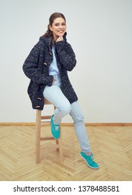 Studio Portrait Of Woman Wearing Sweater Sitting On Stool. Isolated Portrait.