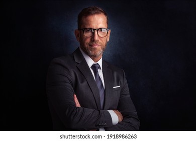 Studio portrait of wrinkle faced businessman wearing suit and tie and looking thoughtfully while standing at isolated dark background. Copy space.