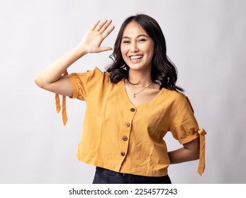A studio portrait of a young beautiful Indonesian Asian woman in a casual suit waving her hand as if saying hai. Isolated on white background. - Powered by Shutterstock