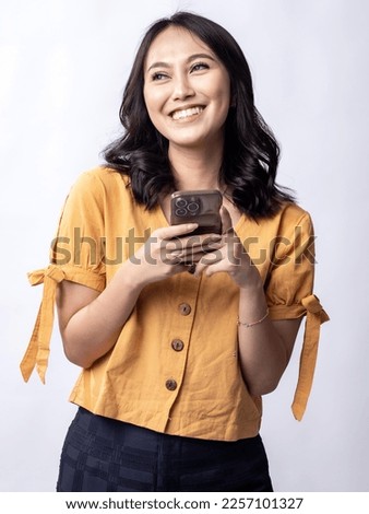 A studio portrait of a young beautiful Indonesian Asian woman in a casual yellow shirt looks happy while typing on her phone.  isolated on white background Foto d'archivio © 