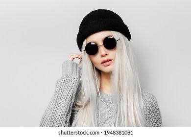 Studio portrait of young blonde girl wearing round sunglasses and black beanie hat on white background.