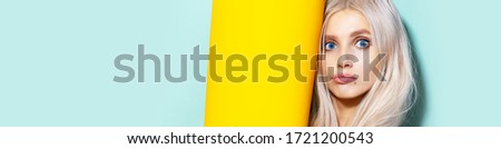 Studio portrait of young blonde girl with blue eyes having fun. Background of aqua menthe color, near yellow. 