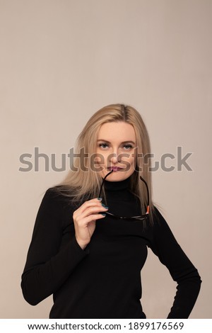 studio portrait of a young blonde girl in a black turtleneck with sunglasses in her hand