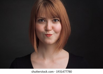 Studio Portrait Of A Young Brown-haired Woman, On A Black Background, Purses Her Lips, Making Duck Lips