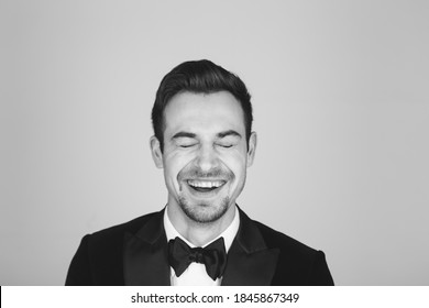 Studio Portrait Of A Young Caucasian Man In A Tuxedo, Laughing Out Loud, Eyes Closed, Against Plain Studio Background