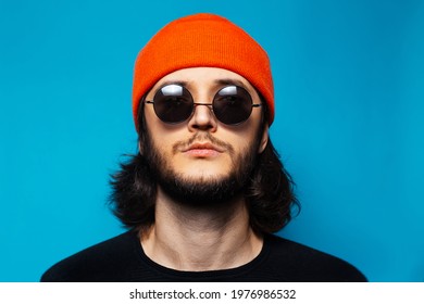 Studio portrait of young confident man on blue background. Guy with long hair wearing orange hat, round sunglasses and black sweater; looking up. - Powered by Shutterstock