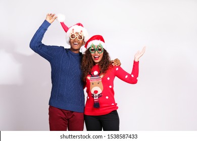 Studio Portrait Of Young Couple, Boyfriend & Girlfriend With Dark Skin Wearing Santa Claus Hat And Christmas Outfit. Ugly Sweater Concept. Close Up, Copy Space For Text, Isolated Background.