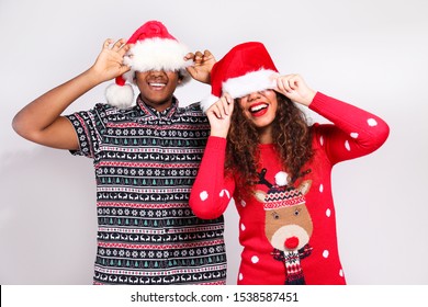 Studio Portrait Of Young Couple, Boyfriend & Girlfriend With Dark Skin Wearing Santa Claus Hat And Christmas Outfit. Ugly Sweater Concept. Close Up, Copy Space For Text, Isolated Background.