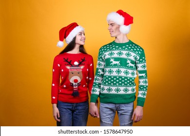 Studio Portrait Of Young Couple, Boyfriend & Girlfriend Wearing Santa Claus Hat & Ugly Christmas Sweater. Holiday Outfit W/ Snowflake Pattern Print. Close Up, Copy Space For Text, Isolated Background.