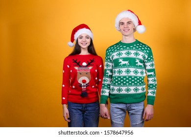 Studio Portrait Of Young Couple, Boyfriend & Girlfriend Wearing Santa Claus Hat & Ugly Christmas Sweater. Holiday Outfit W/ Snowflake Pattern Print. Close Up, Copy Space For Text, Isolated Background.