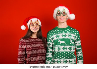 Studio Portrait Of Young Couple, Boyfriend & Girlfriend Wearing Santa Claus Hat & Ugly Christmas Sweater. Holiday Outfit W/ Snowflake Pattern Print. Close Up, Copy Space For Text, Isolated Background.