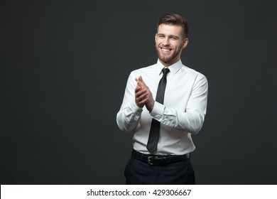 Studio portrait of young happy handsome businessman clapping hands isolated on dark background. - Powered by Shutterstock