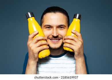 Studio Portrait Of Young Joyful Man, Holding Two Yellow Eco Bottles Close To His Face.