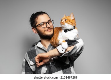 Studio portrait of young smiling man with red cat on his arms. Grey background.