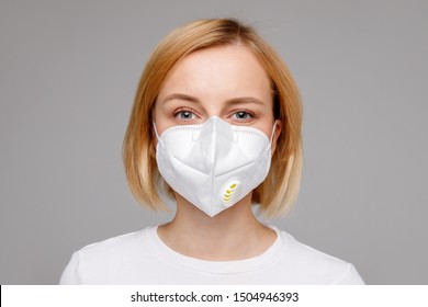 Studio portrait of young woman wearing a face mask, looking at camera, close up, isolated on gray background. Flu epidemic, dust allergy,  protection against virus. City air pollution concept 