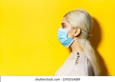 Studio Profile Portrait Of Young Blonde Girl, Wearing Flu Medical Mask On Yellow Background With Copy Space.