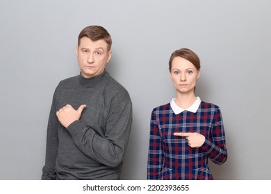 Studio shot of adult couple, disappointed man and serious focused woman are pointing at each other. Concept of relationship, interaction between people, gender relations, communication issues