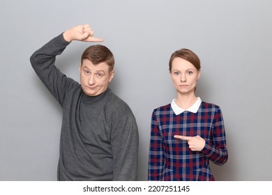 Studio Shot Of Adult Couple, Disappointed Man And Serious Focused Woman Are Pointing At Each Other. Concept Of Relationship, Interaction Between People, Gender Relations, Communication Issues