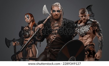 Studio shot of ancient vikings with fur and axes against gray background.