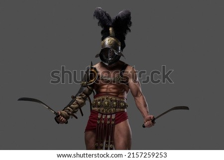 Studio shot of antique gladiator with muscular build and two swords isolated on gray background.