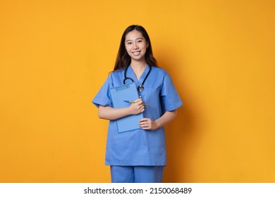 Studio shot of an asian doctor in uniform holding a folder while smiling in a orange background