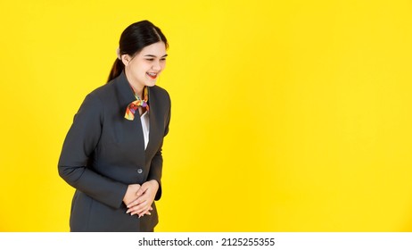 Studio shot of Asian professional successful female flight attendant air hostess in formal uniform wearing teeth braces standing smiling bowing head down greeting passenger on yellow background.