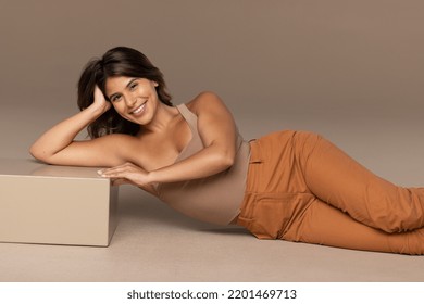 studio shot of attractive hispanic woman in her 20s laying on blocks posing seductively and smiling on neutral background Stock Photo