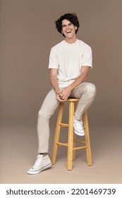 studio shot of attractive young latino man in his 20s sitting on stool and smiling on neutral background Stock Photo