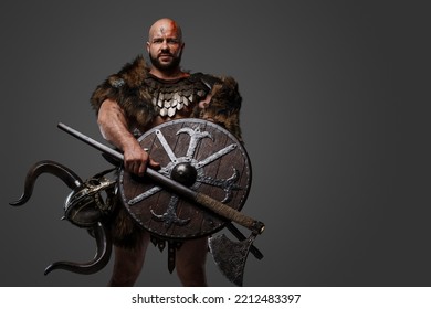 Studio Shot Of Barbaric Viking With Bloody Face Holding Shield And Axe Isolated On Grey.
