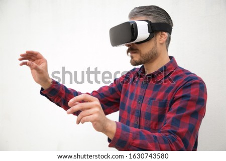 Studio shot of bearded man testing virtual reality headset. Focused young tester experiencing VR glasses. Technology concept