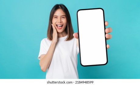 Studio shot of Beautiful Asian woman holding smartphone mockup of blank screen and smiling on blue background. - Shutterstock ID 2184948599