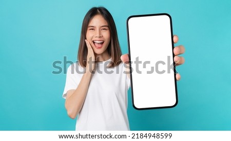 Studio shot of Beautiful Asian woman holding smartphone mockup of blank screen and smiling on blue background.