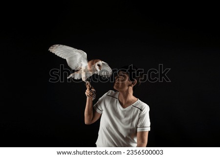 Studio shot of a beautiful baby owl with its wings outstretched and held by a woman. Wild animal. Isolated on black color background.