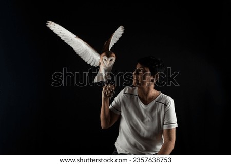 Studio shot of a beautiful baby owl with its wings outstretched and held by a woman. Wild animal. Isolated on black color background.
