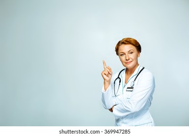 Studio Shot Of Beautiful Redheaded Female Doctor. Medical Worker With Stethoscope Smiling, Pointing Up And Looking At Camera