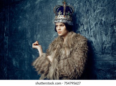 Studio shot of beautiful young woman in crown  and fur coat  at dark studio background 