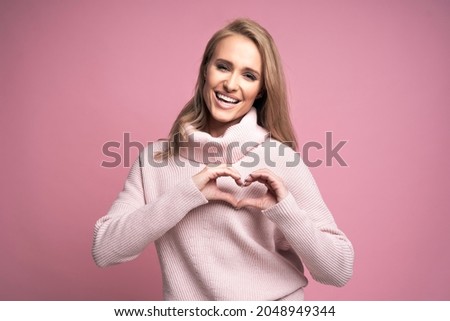 Studio shot of cheerful caucasian young woman making a heart sign with her hands