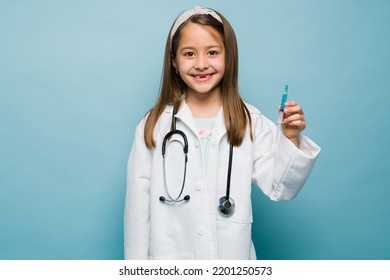 Studio Shot Of A Cheerful Little Girl Playing Doctor Holding A Syringe To Give A Vaccine Shot And Having A Career Aspiration