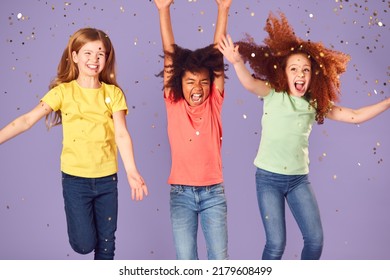 Studio Shot Of Children With Glitter Jumping In The Air With Outstretched Arms On Purple Background
