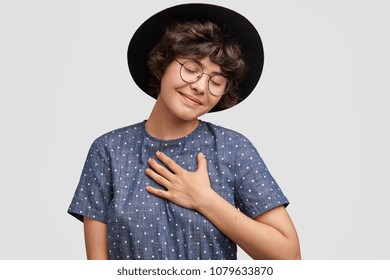 Studio Shot Of Delighted Pleased Female Student Keeps Hand On Chest As Being Satisfied To Hear Heart Piercing Story From Male Groupmate, Keeps Eyes Shut, Glad Recieve Compliment From Stranger