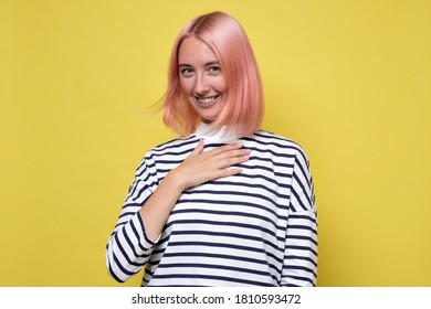 Studio Shot Of Delighted Pleased Female Student Keeps Hand On Chest As Being Satisfied To Hear A Compliment From Stranger