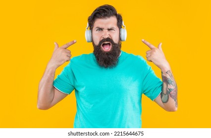 Studio Shot Of Displeased Annoyed Man By Loud Music. Annoyed Man Has Loud Music In Headphones