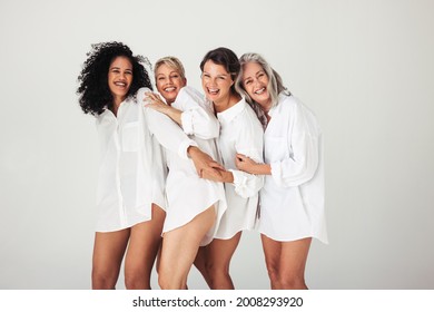 Studio Shot Of Diverse Female Models Embracing Their Natural And Ageing Bodies. Four Confident And Happy Women Smiling Cheerfully While Wearing White Shirts Against A White Background.