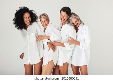 Studio shot of diverse women embracing their natural and aging bodies. Four confident and happy women smiling cheerfully while wearing white shirts against a white background.