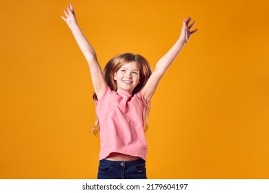 Studio Shot Of Energetic Boy Girl In The Air With Outstretched Arms Against Yellow Background