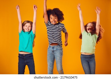 Studio Shot Of Energetic Children Jumping In The Air With Outstretched Arms On Yellow Background