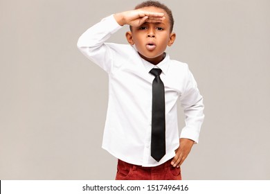 Studio shot of excited stylish African schoolboy having astohished surprised facial expression, holding hand at his forehead as if looking into distance at something curious. Body langauge