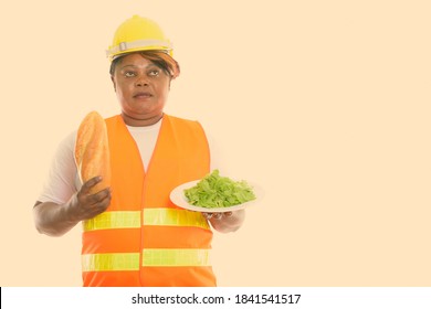 Studio Shot Of Fat Black African Woman Construction Worker Thinking While Holding Bread And Lettuce Served On White Plate