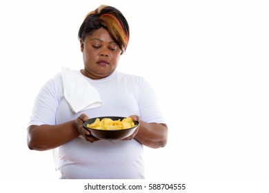 Studio shot of fat black African woman holding and looking at bowl of potato chips
