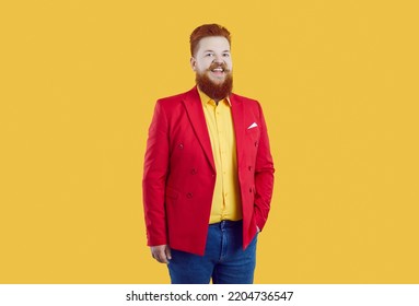 Studio Shot Of Fat Redhead Guy In Funny Outfit. Happy Cheerful Chunky Man Wearing Bright Red Suit Jacket, Yellow Shirt And Blue Jeans Standing Isolated On Yellow Background. Funny Fashion Concept